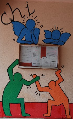 Murales sul lato sinistro dell'ingresso secondario del plesso centrale. I disegni, simili a quelli dell'artista statunitense Keith Haring, rappresentano degli omini che reggono la bacheca esterna. Sopra la bacheca un altro disegno con due angioletti stilizzati